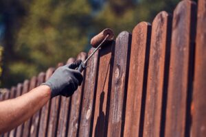 man-protective-gloves-is-painting-wooden-fence-bright-summer-day.jpg  